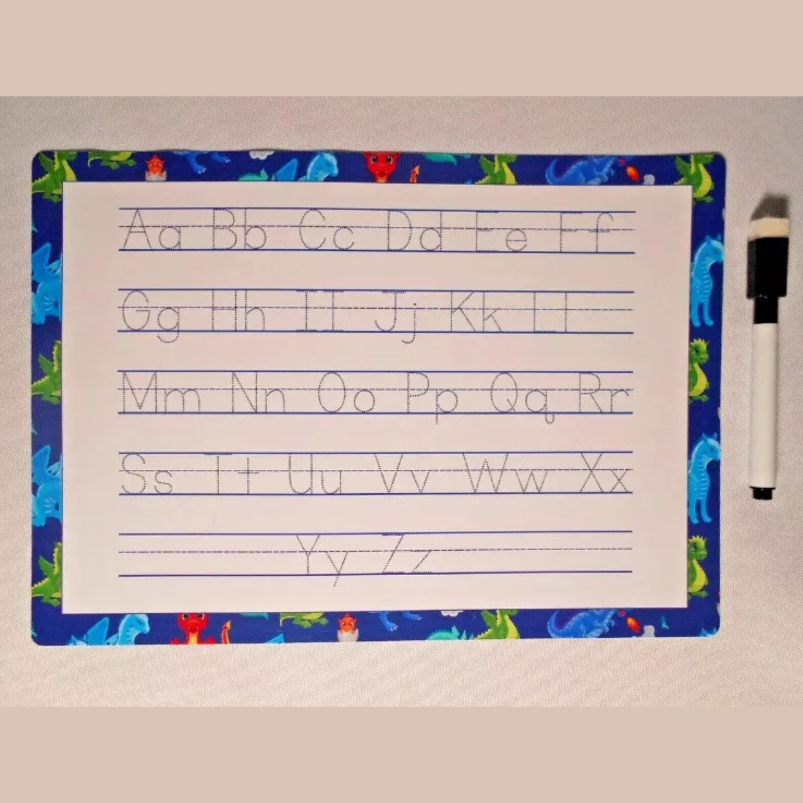 Alphabet tracing sheet with uppercase and lowercase letters on a dinosaur-pattern mat with marker for kids.